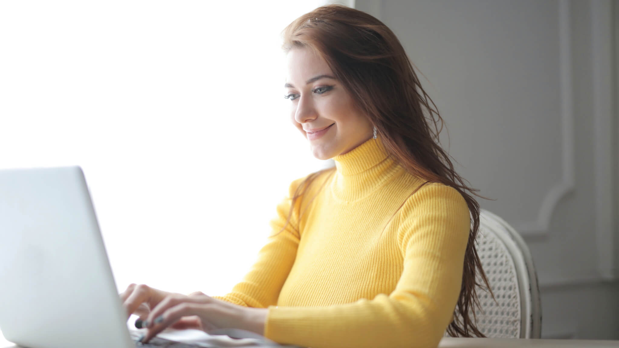 Woman with yellow sweater smiling at laptop